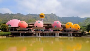 A building with multiple spherical structures, a central tower, and a body of water in the foreground. - DNA Super Ozone Resort KhaoYai (Pak Chong)