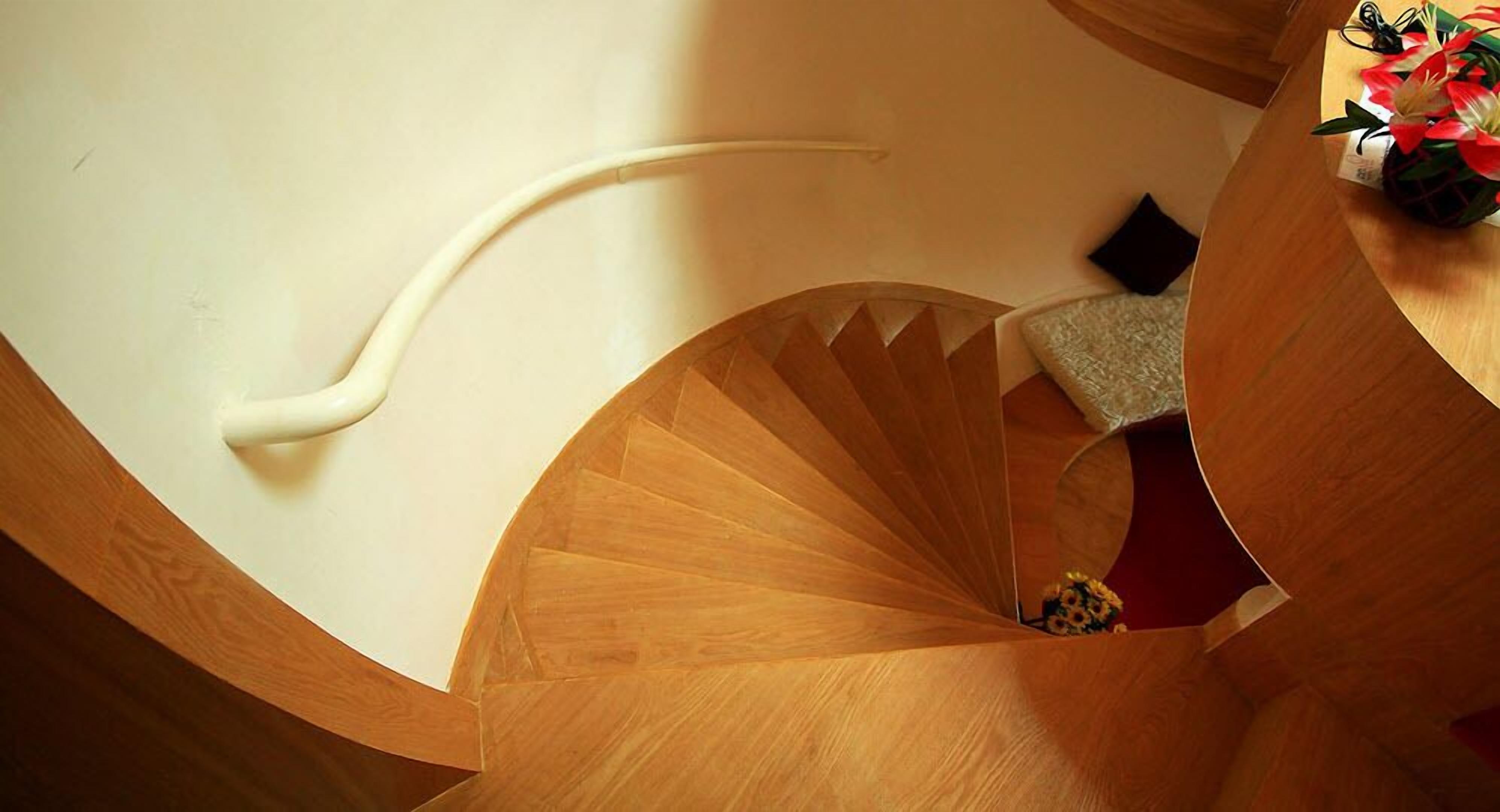 A spiral staircase with a wooden finish and a red carpet at the bottom.