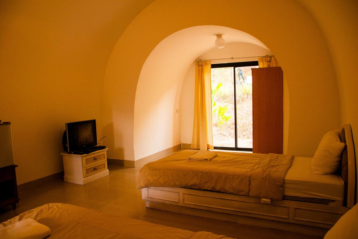 A bedroom with a bed, a TV on a stand, and a window with curtains.