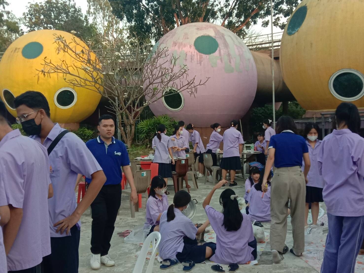 A group of people in school uniforms gathered around large, colorful spherical structures.