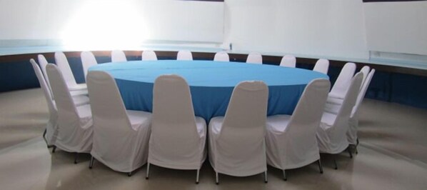 A conference room with a round table covered in a blue tablecloth, surrounded by white chairs.
