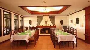 Ein Esszimmer mit langen Tischen, die für eine Mahlzeit gedeckt sind, einem Kamin und einer Chandelüster.