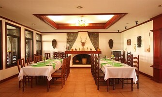 Un comedor con mesas largas dispuestas para una comida, chimenea y candelabro.