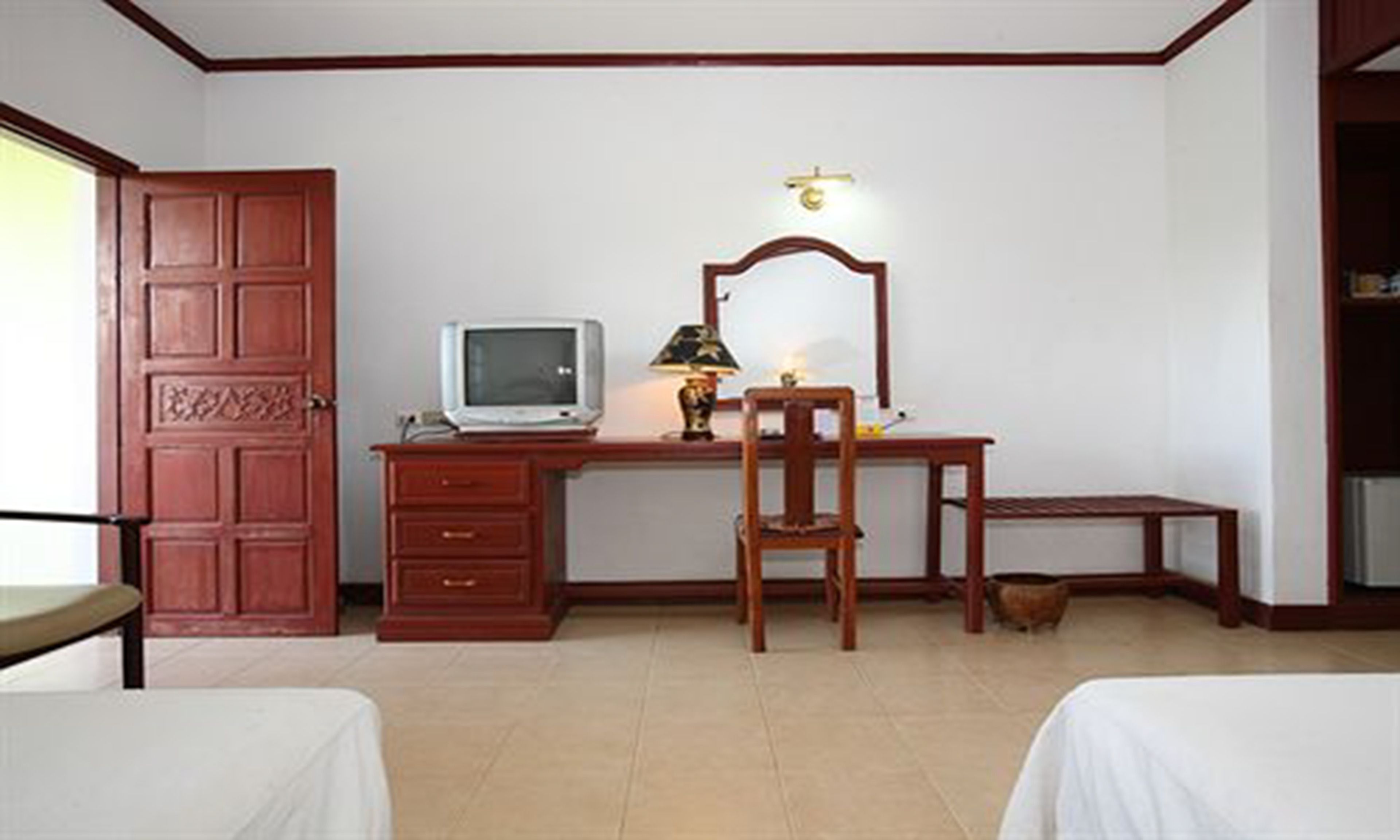 A room with a wooden desk, a chair, a television, and a bed.