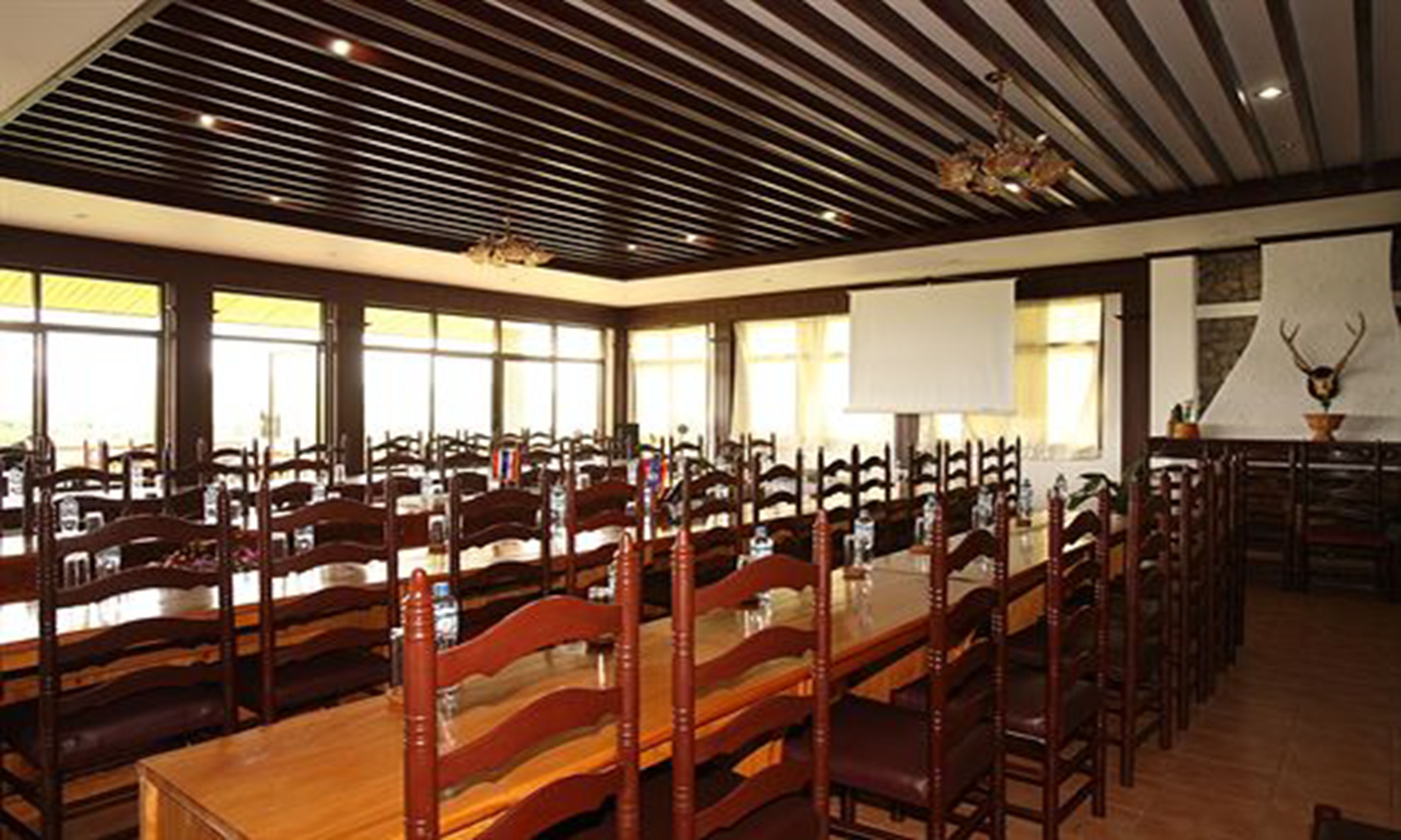 A conference room with long tables and wooden chairs, large windows, and a ceiling with wooden beams.