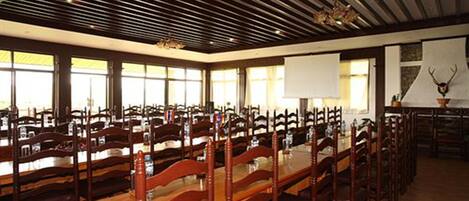 A conference room with long tables and wooden chairs, large windows, and a ceiling with wooden beams.