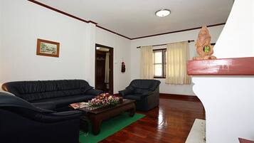 A living room with a dark-colored sofa, a smaller armchair, a wooden coffee table with flowers, a green rug, and a white wall with a framed picture.