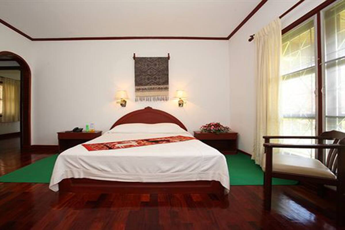 Un dormitorio con una cama de madera, una alfombra verde, una silla y un tapiz colgado en la pared.