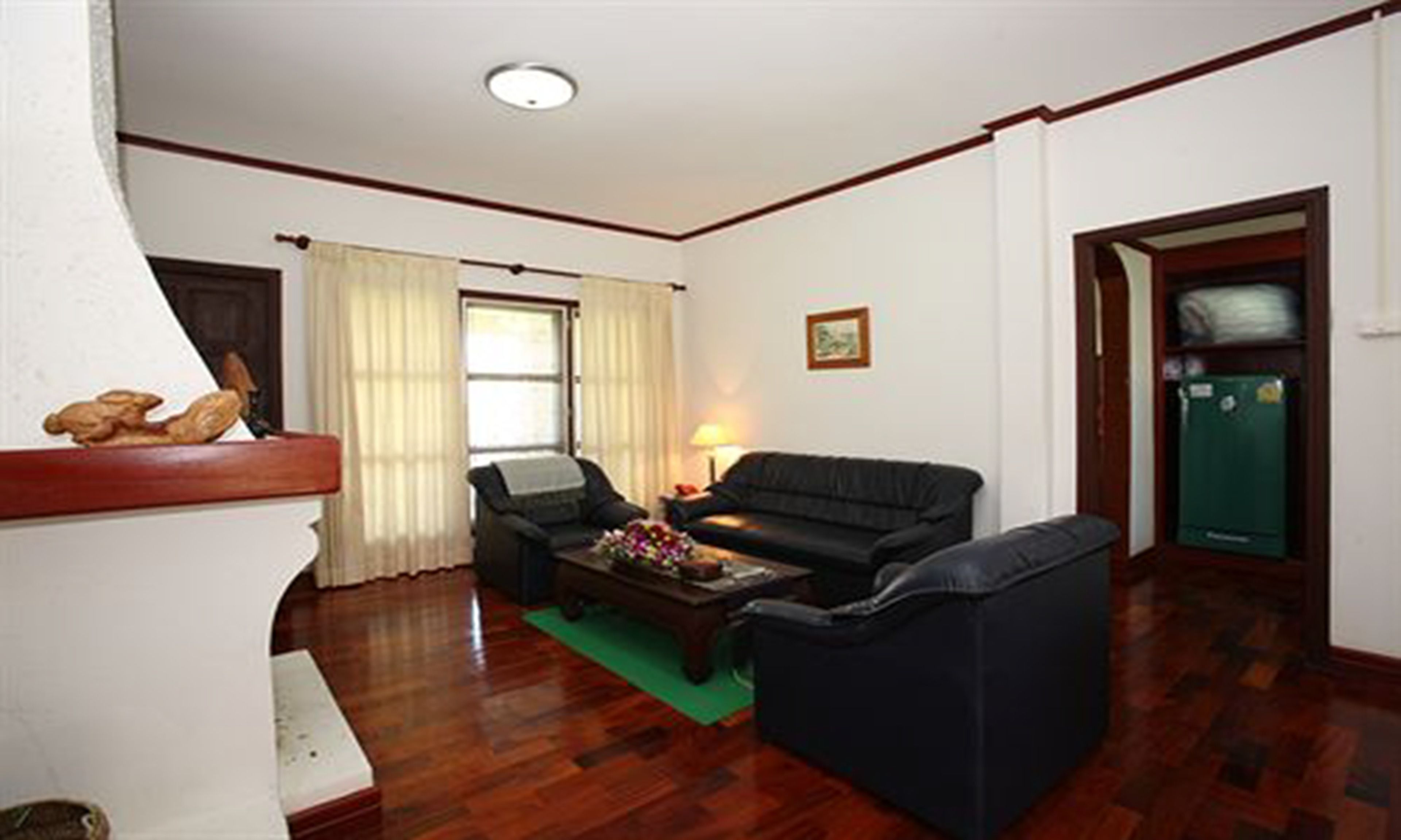 A living room with a sofa, a coffee table, and a lamp. There is a window with curtains and a door to the right.