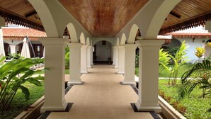 A covered corridor with white columns and a wooden ceiling, leading to a building entrance.