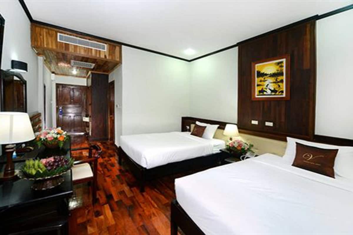 A hotel room with two beds, a desk with a lamp, a chair, and a wooden floor.