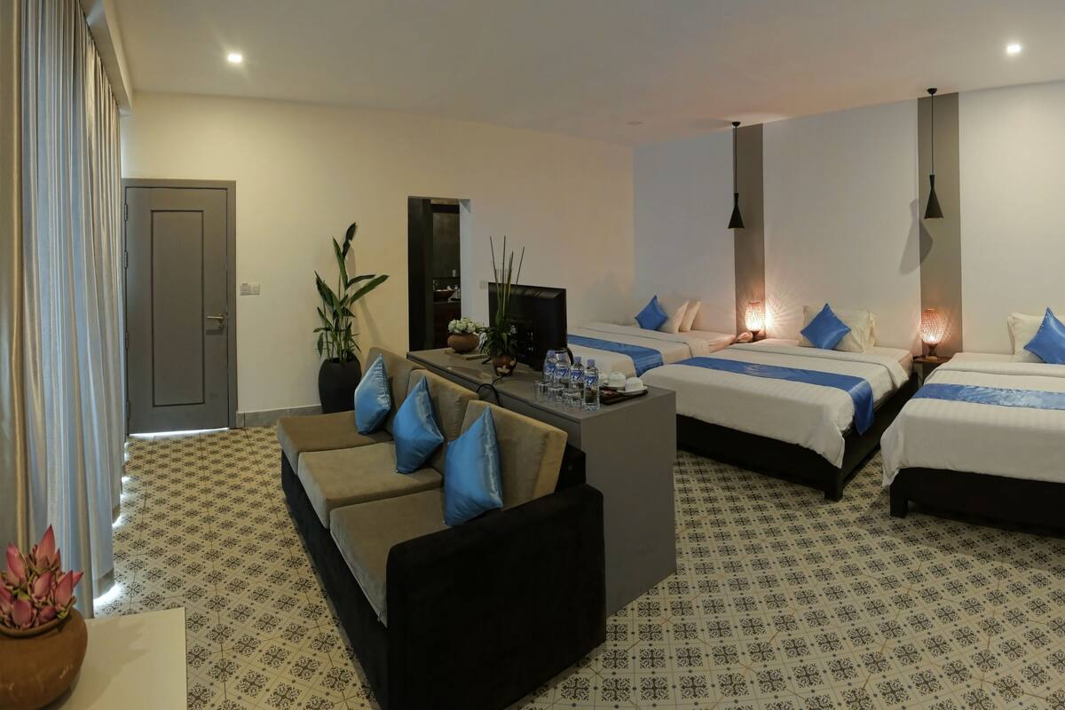Habitación de hotel con dos camas, un sofá, un televisor y una mesita con botellas de agua.