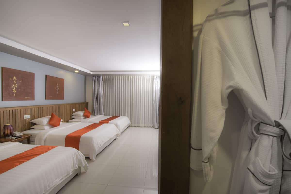 Habitación de hotel con tres camas, cabecera de madera, ropa de cama blanca y almohadones naranjas.