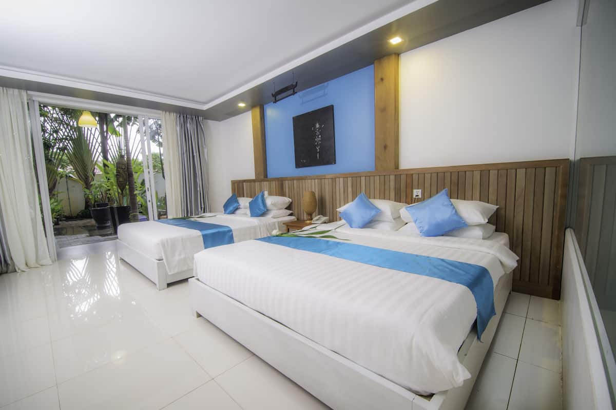 Habitación de hotel con dos camas, una pared azul y vistas a la vegetación.