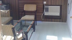 A room with a glass-top table, striped chairs, a framed picture, and a wall-mounted air conditioner. - Hotel TARA International (Hyderabad)