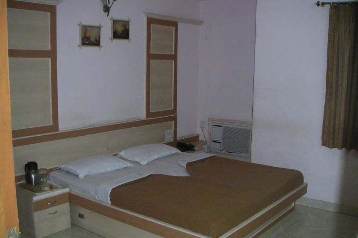 Un llit individual estàndard amb capçalera de fusta, una taula de nit i una petita taula al costat del llit. Hi ha una finestra amb vista a l'exterior i un aire condicionat fixat a la paret.