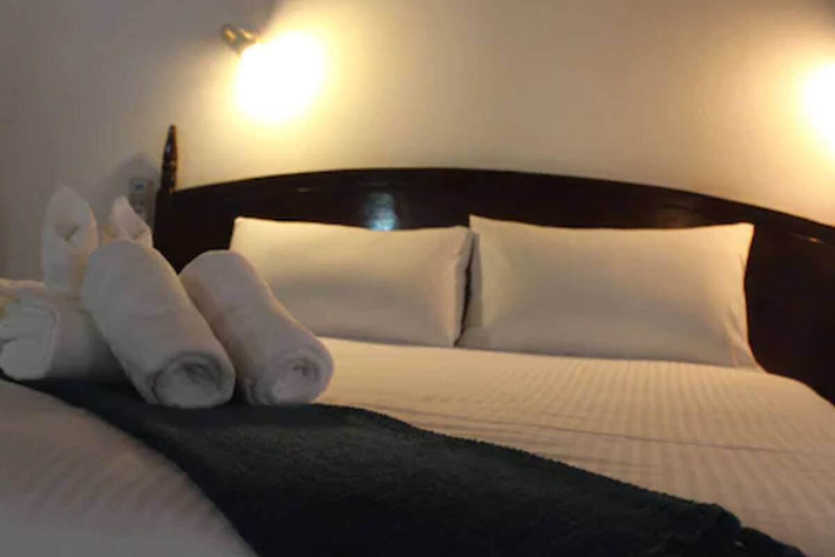 A neatly made bed with white linens and pillows, a dark headboard, and two wall-mounted lights.