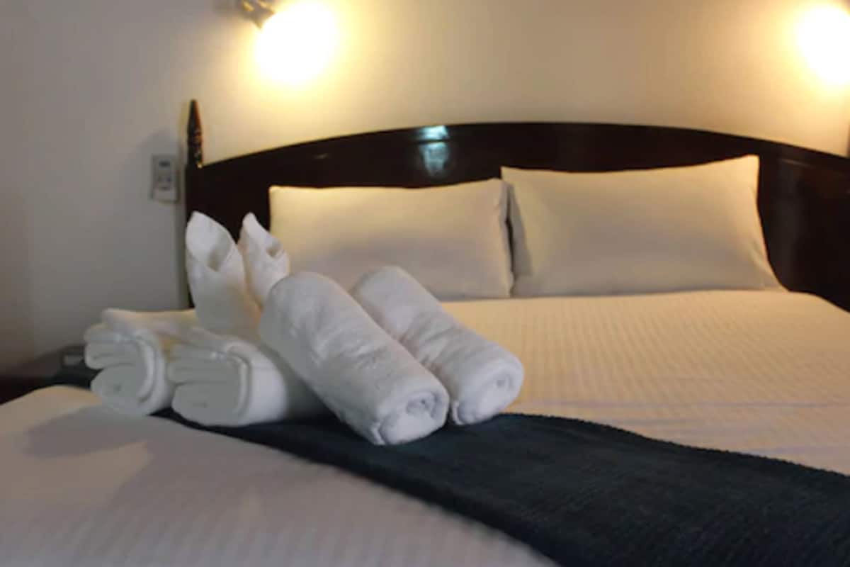 A neatly made bed with white linens and pillows, a folded towel on the side, and a dark headboard.