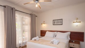 A hotel room with a bed, curtains, a ceiling fan, a wall-mounted light, and a framed picture. - Pamusha Lodge (Victoria Falls)