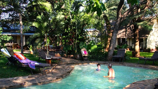 A pool area with lounge chairs and a clear pool surrounded by tropical vegetation. - Pamusha Lodge (Victoria Falls)