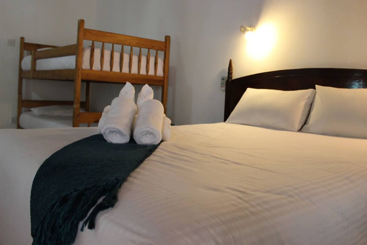 A hotel room with a bed, a wooden bunk bed, and a wall-mounted light.