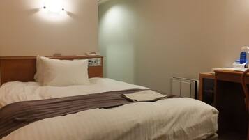 A hotel room with a bed, bedside table, and a small desk with a chair.
