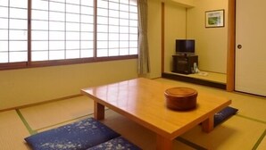 Una habitación japonesa tradicional con suelo de tatami, una mesa de madera, un televisor y puertas correderas.