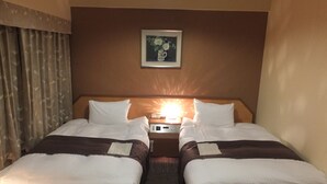Habitación de hotel con dos camas, una mesita de noche con lámpara y un cuadro enmarcado en la pared.