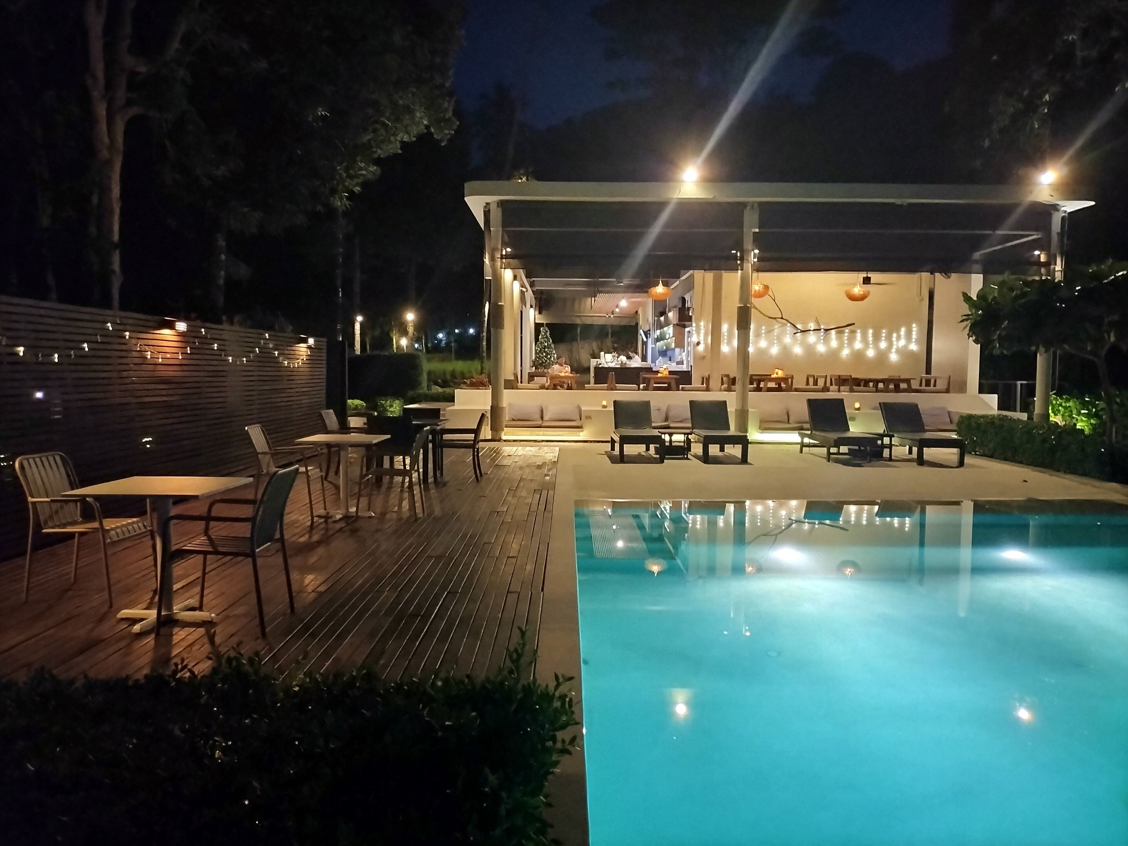 An outdoor pool area with lounge chairs and tables, a covered seating area, and a bar.