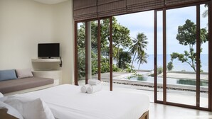 Une chambre moderne dotée d’un grand lit, d’un téléviseur à écran plat et offrant une vue sur une piscine et un paysage tropical.