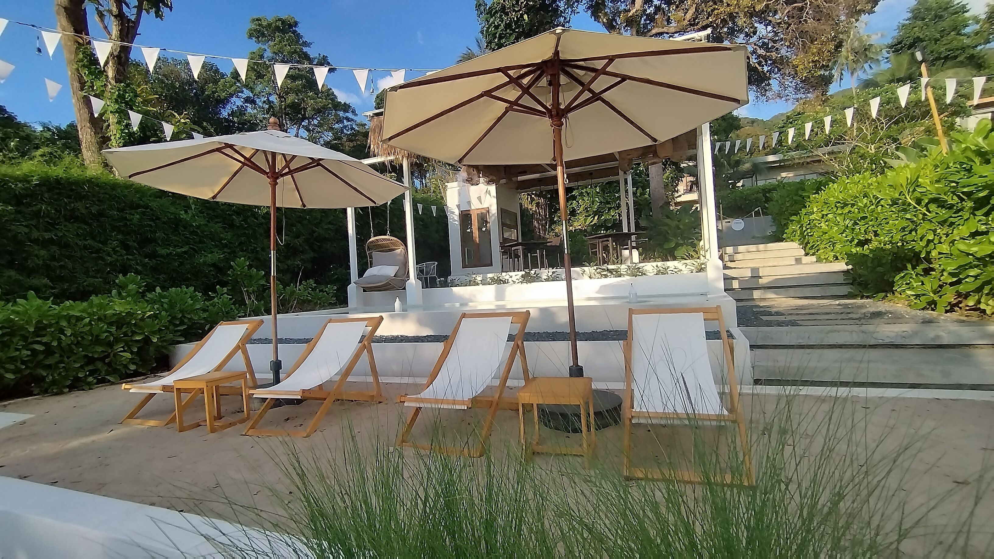 A patio area with lounge chairs and umbrellas, a pergola, and a view of a building in the background.