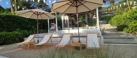 A patio area with lounge chairs and umbrellas, a pergola, and a view of a building in the background.