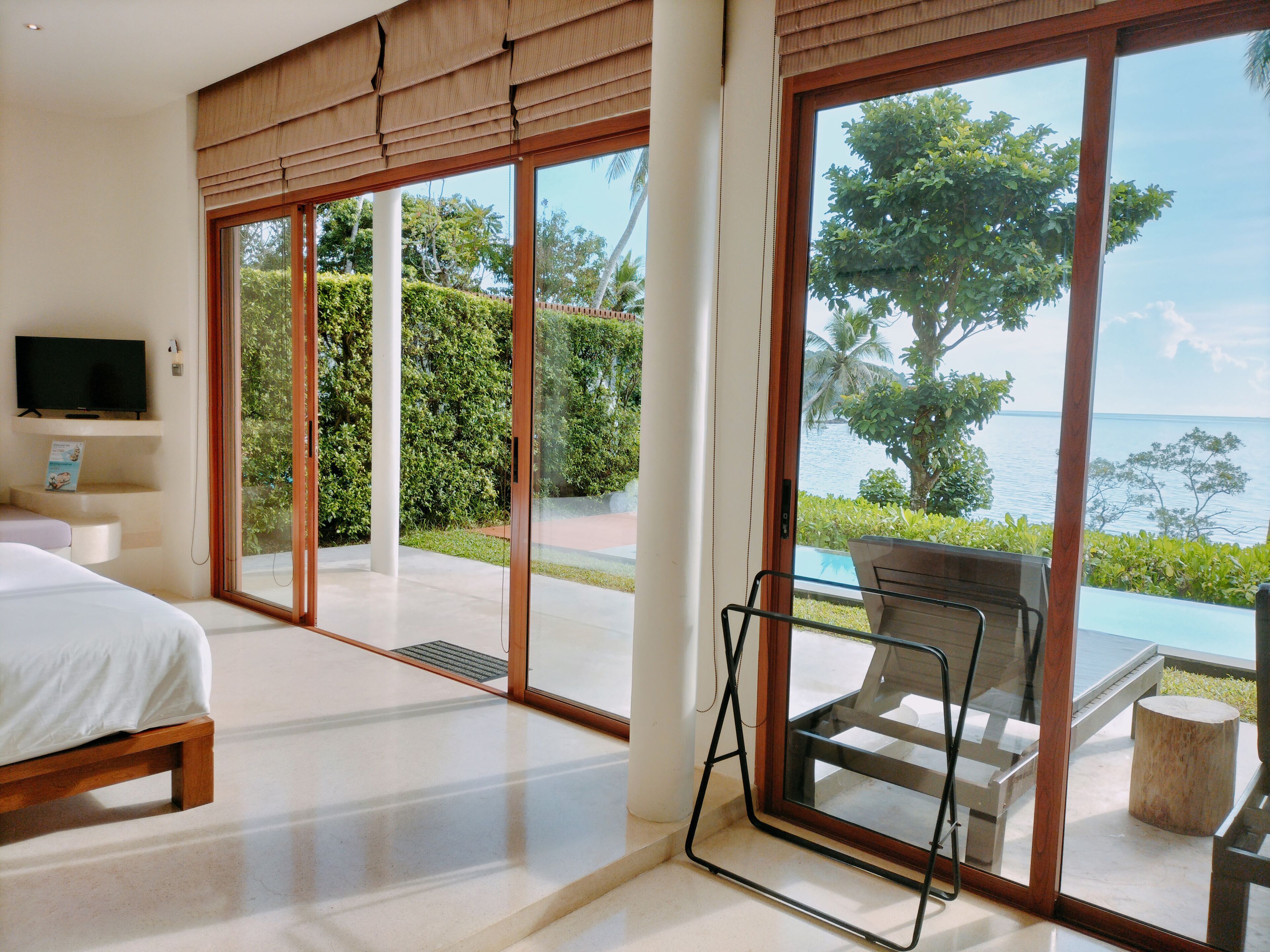 Un dormitorio moderno con una cama grande, televisor y vistas a una piscina y vegetación.