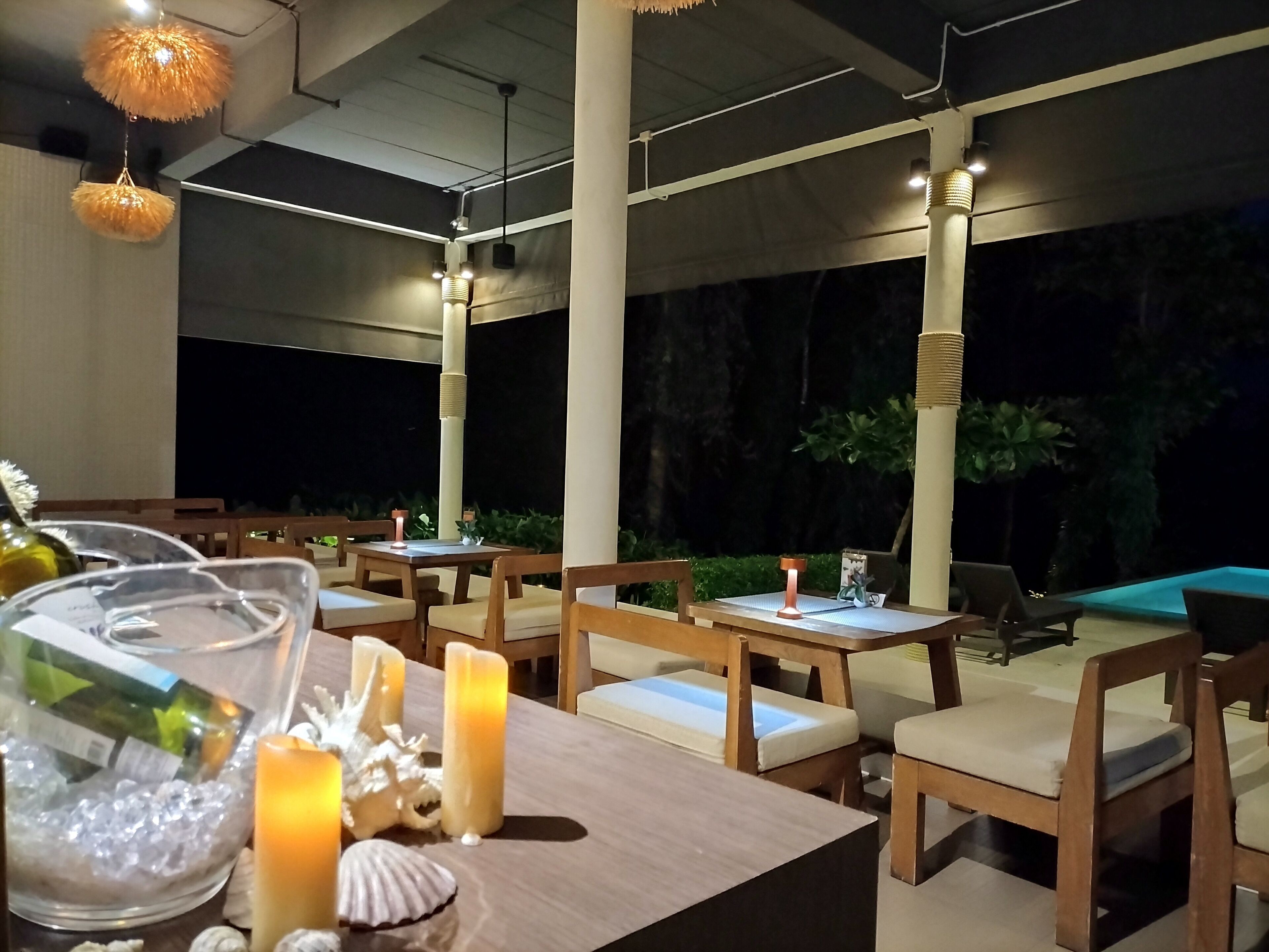 Een terras met houten tafels en stoelen, kaarsen en decoratieve elementen.