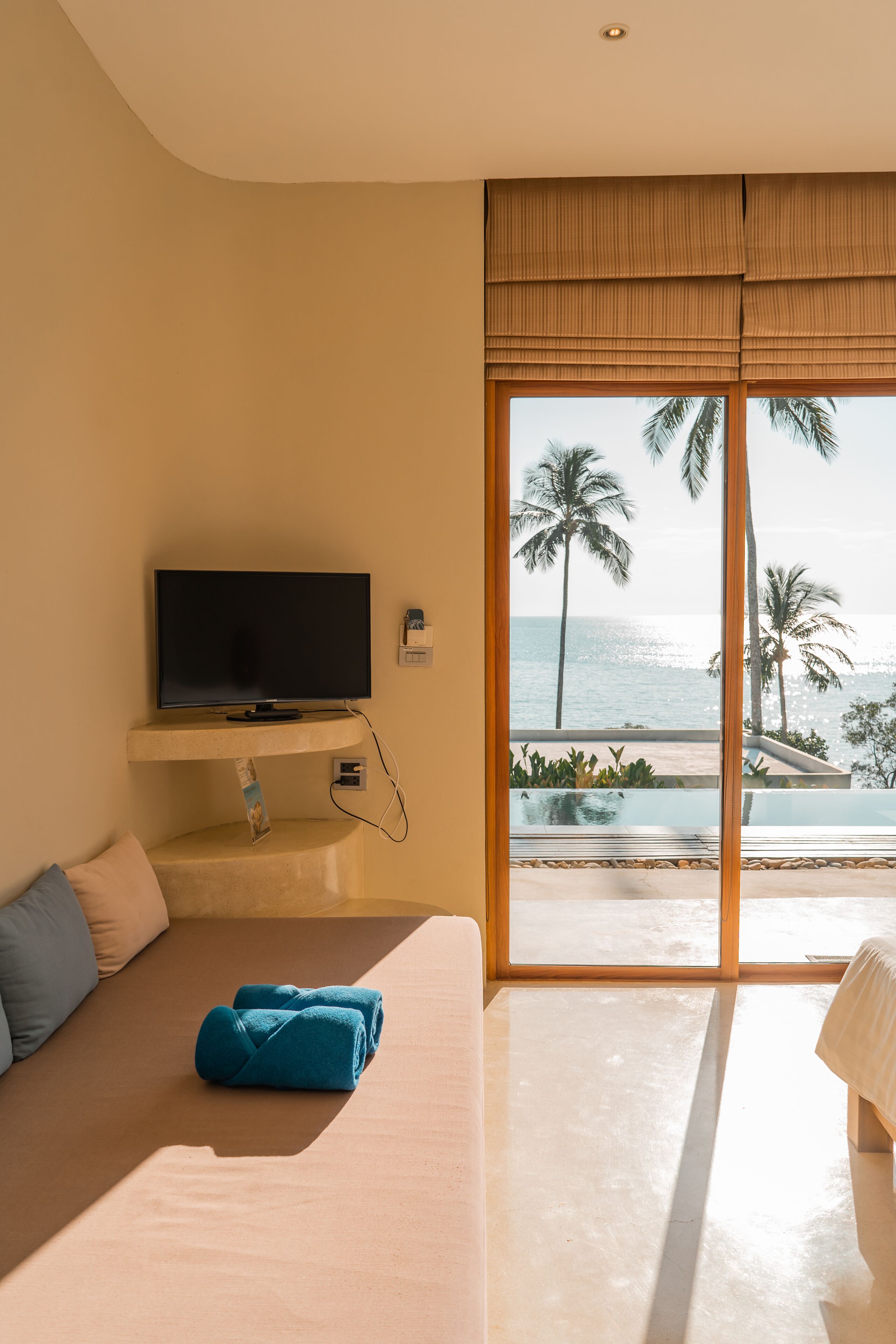 A modern hotel room with a large window, a flat-screen TV, a sofa, and a neatly made bed.