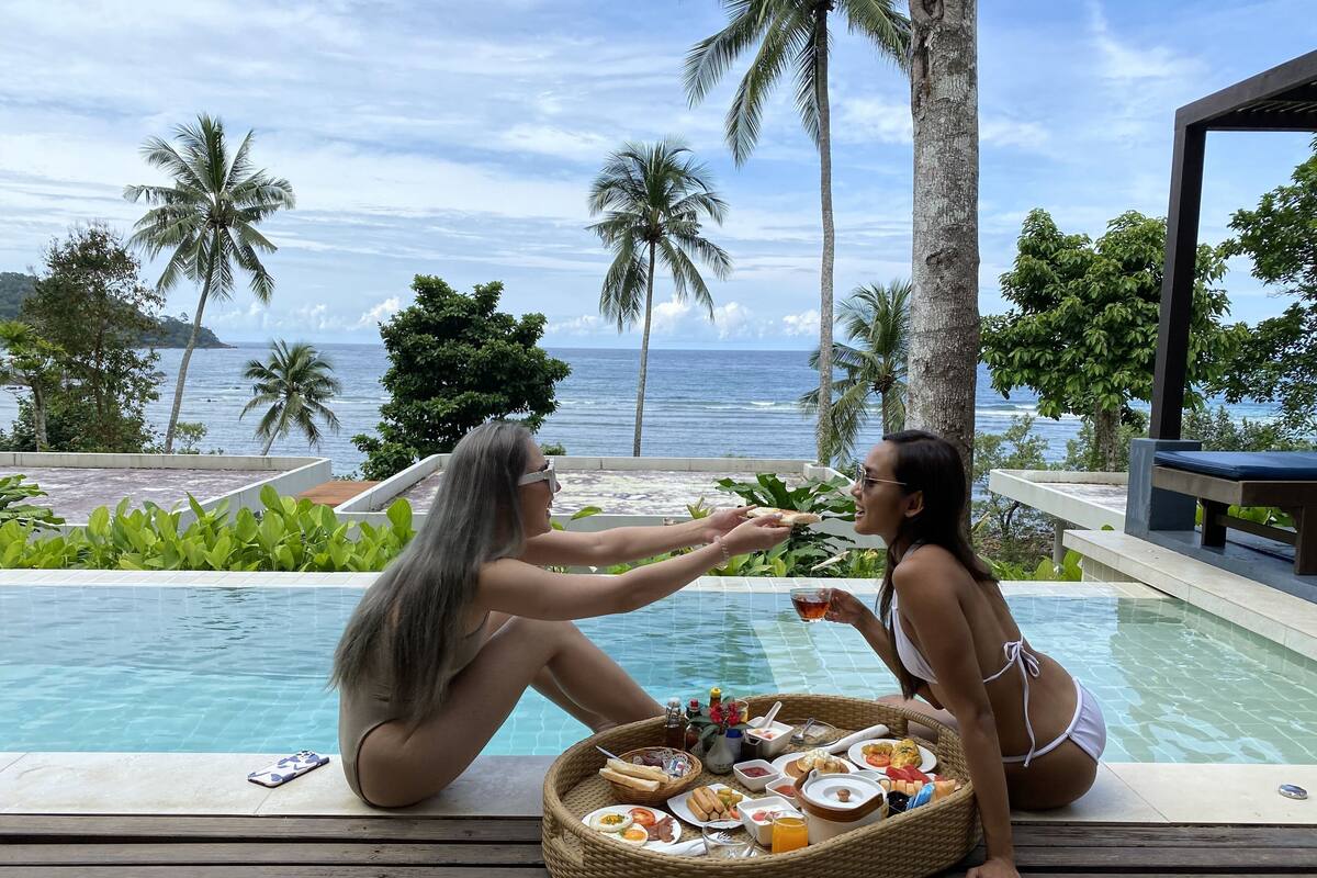 A poolside setting with a dining setup featuring a basket of food, a drink, and a smartphone on the edge of the pool.