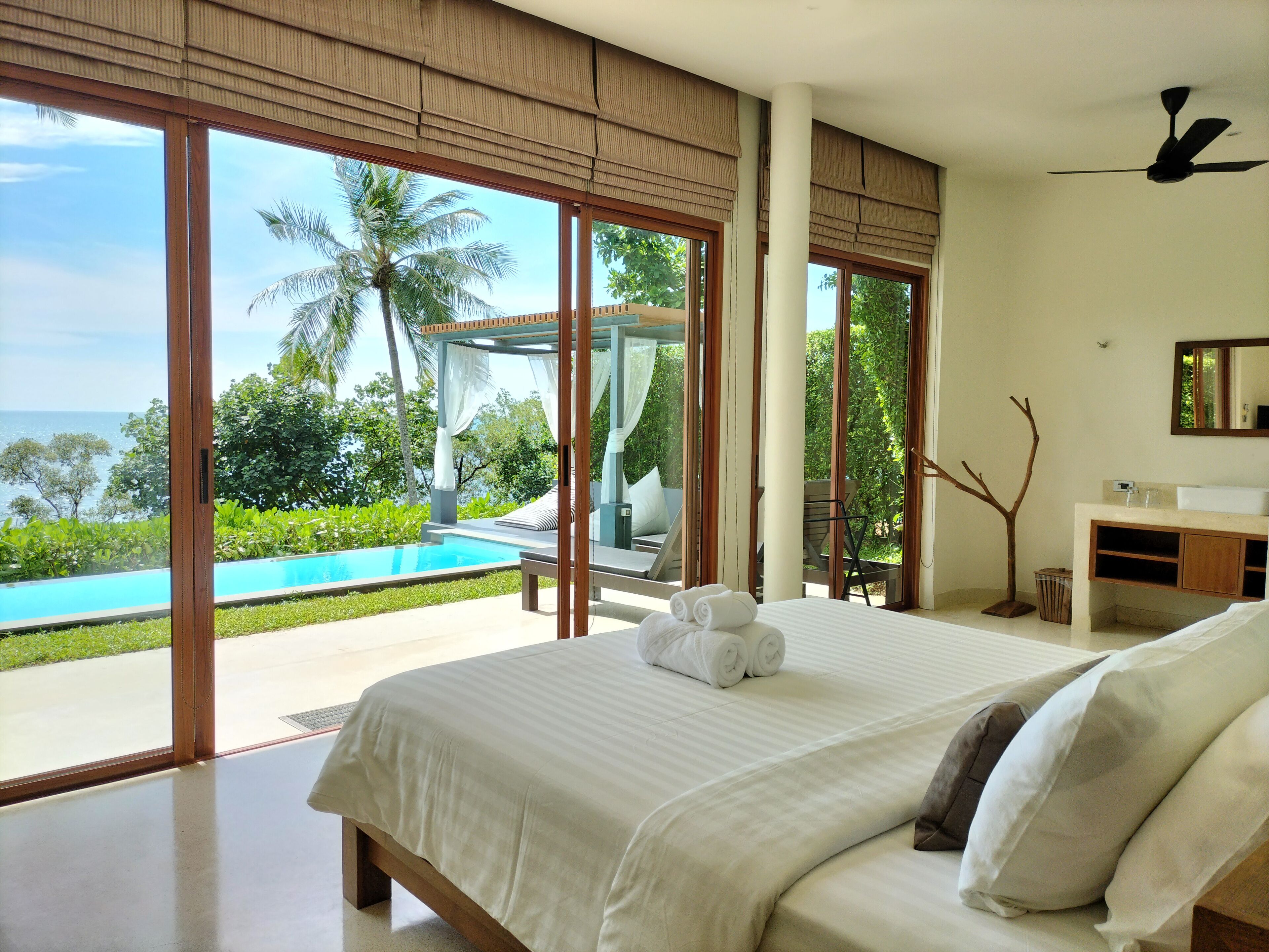 Un dormitorio con una cama grande, vista a una piscina y un baño con espejo y lavabo.