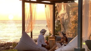 Un couple se détend au bord d’une piscine, avec une vue sur l’océan au coucher du soleil.