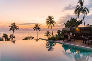 An infinity pool with a view of the ocean and palm trees at sunset. - Nest Sense Resort (Ko Chang)