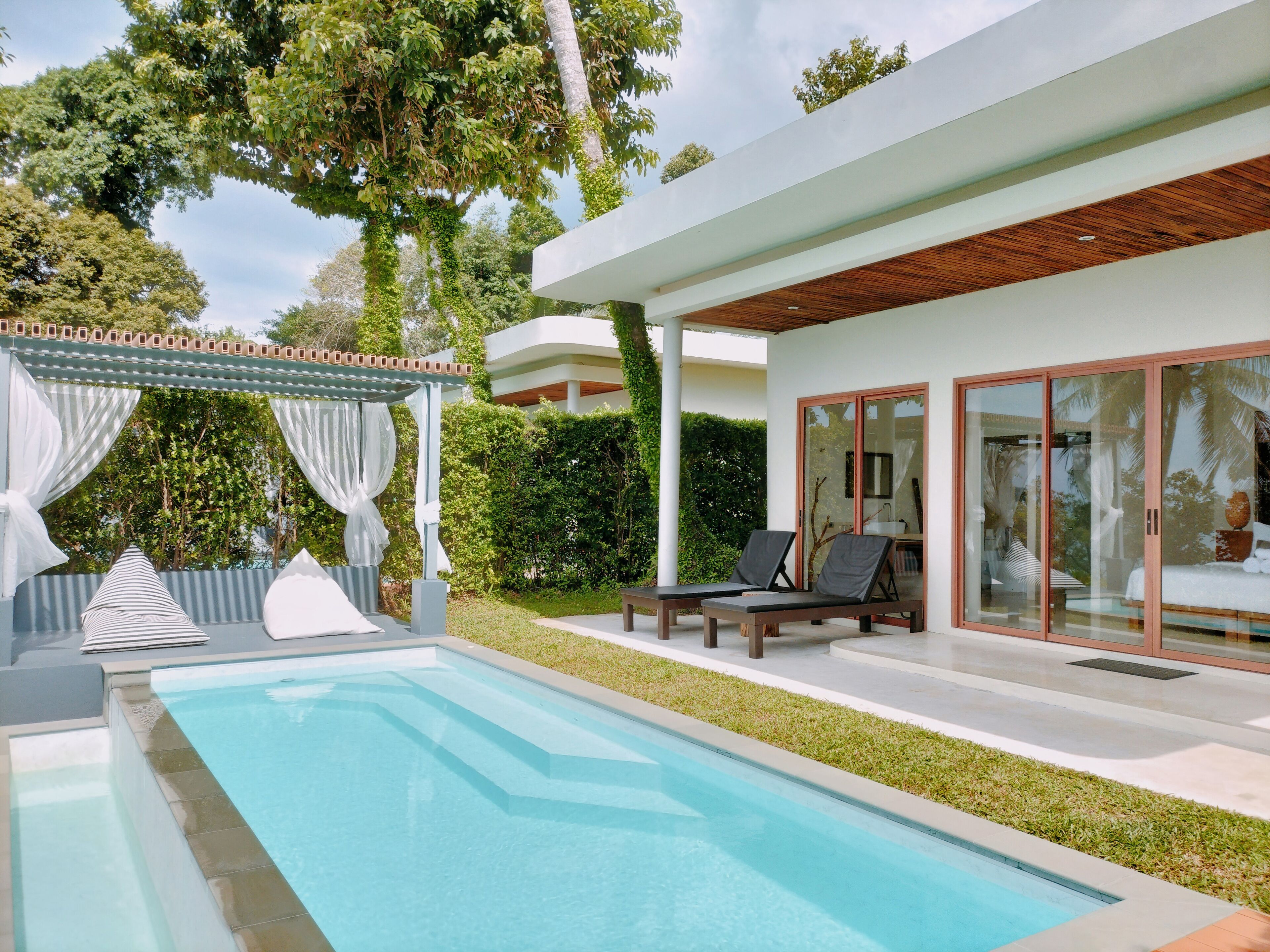 Ein moderner Poolbereich mit klarem Pool, Liegestühlen und einer überdachten Sitzgruppe.