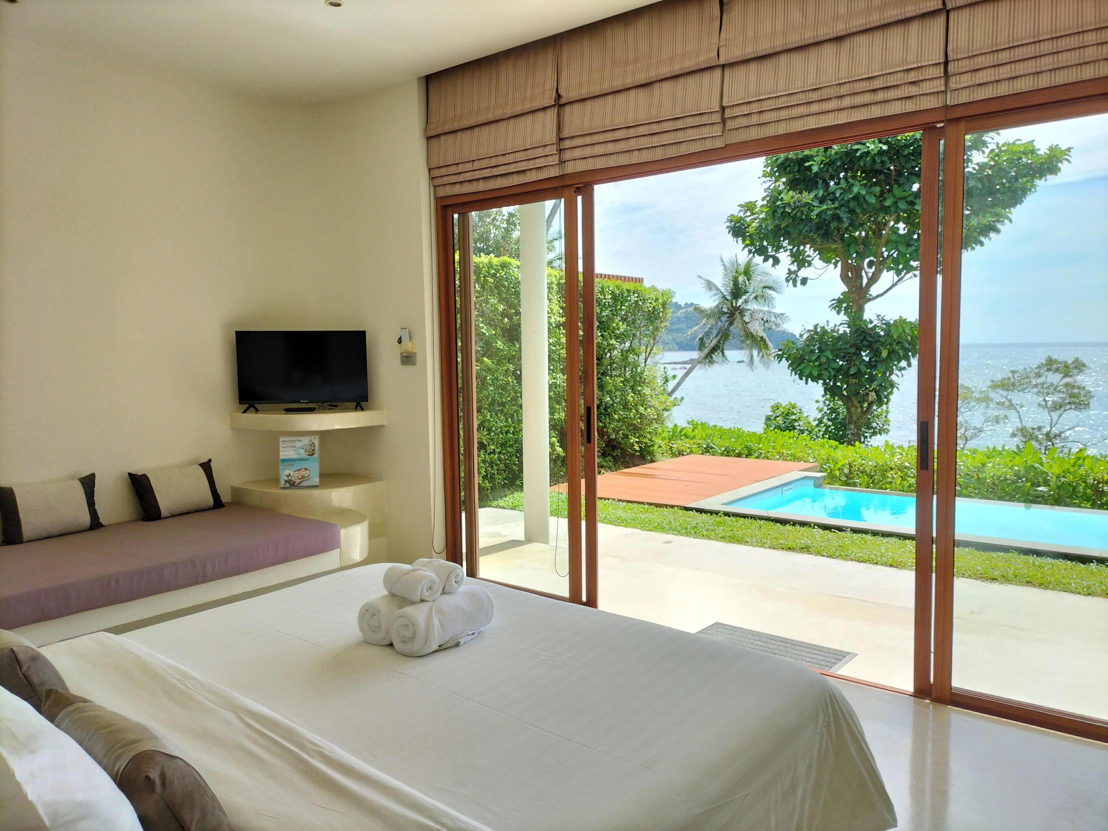 Habitación de hotel con cama, televisor y vista a una piscina y al océano.