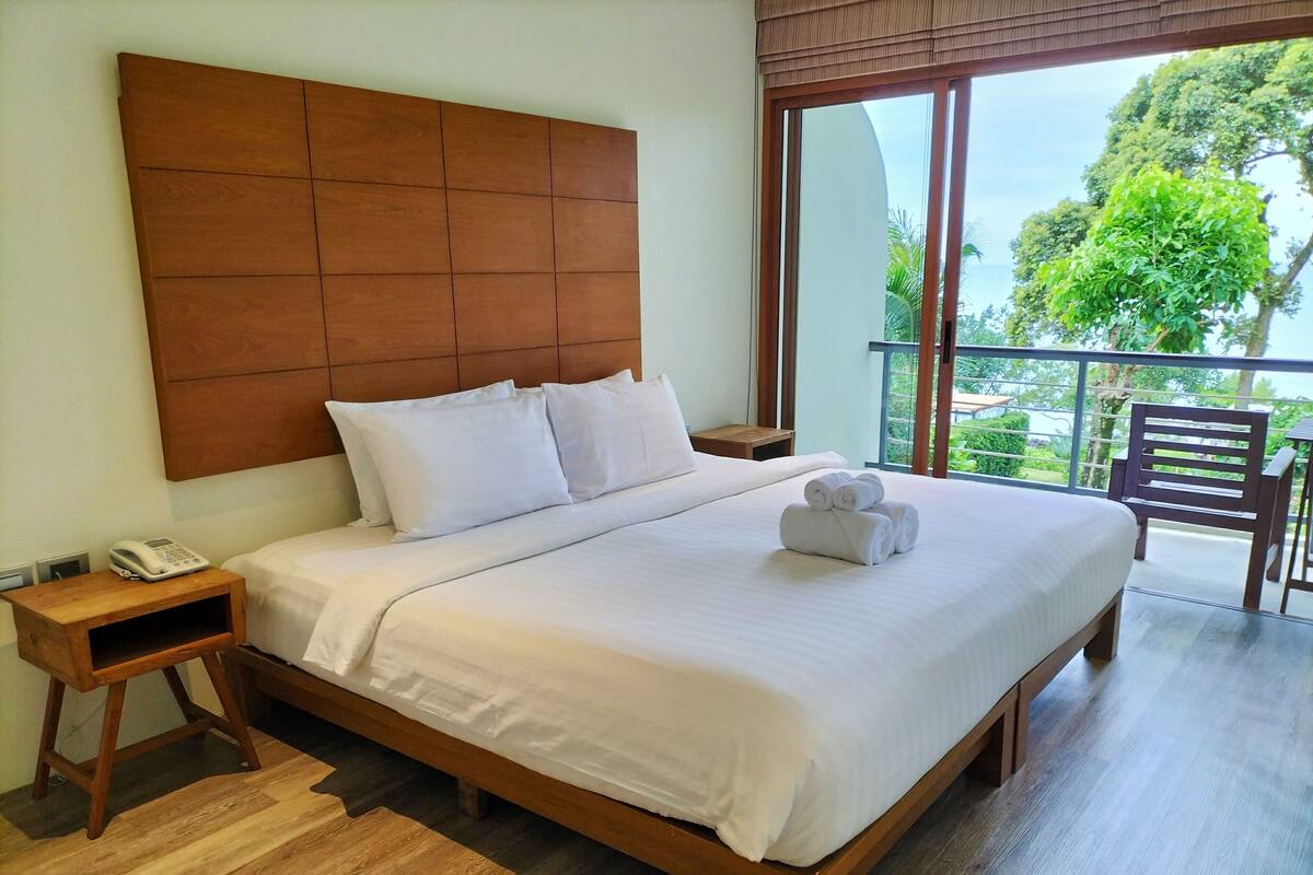 A neatly made bed with white linens and pillows, a wooden headboard, a bedside phone, and a small wooden nightstand.