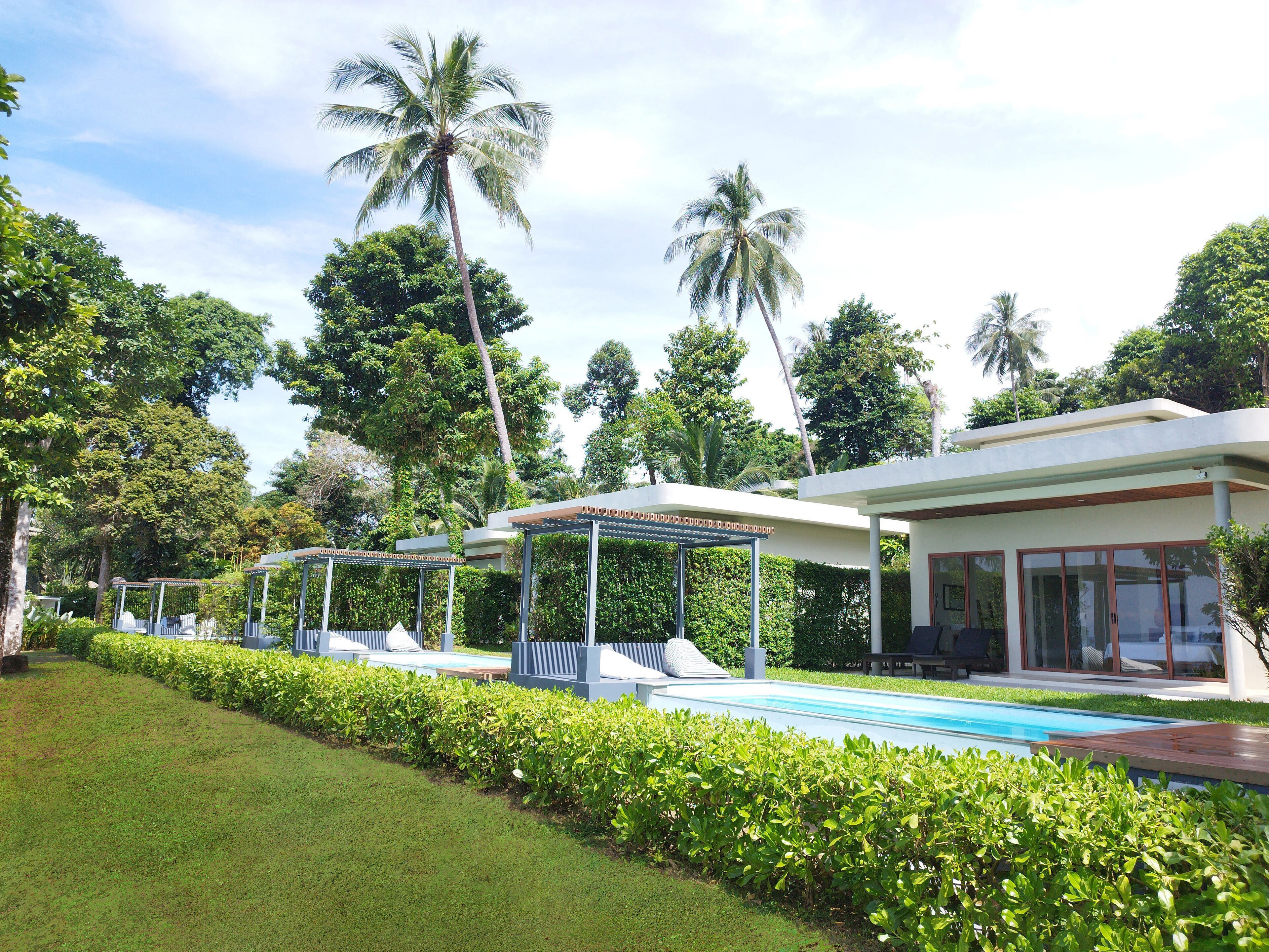 A pool area with lounge chairs, a covered seating area, and a modern building with large windows.