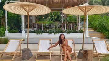 Relax in a serene outdoor lounge surrounded by lush greenery and a body of water.