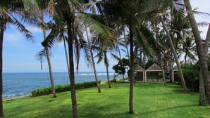 Un resort tropical con vista despejada al océano, palmeras y un pabellón.