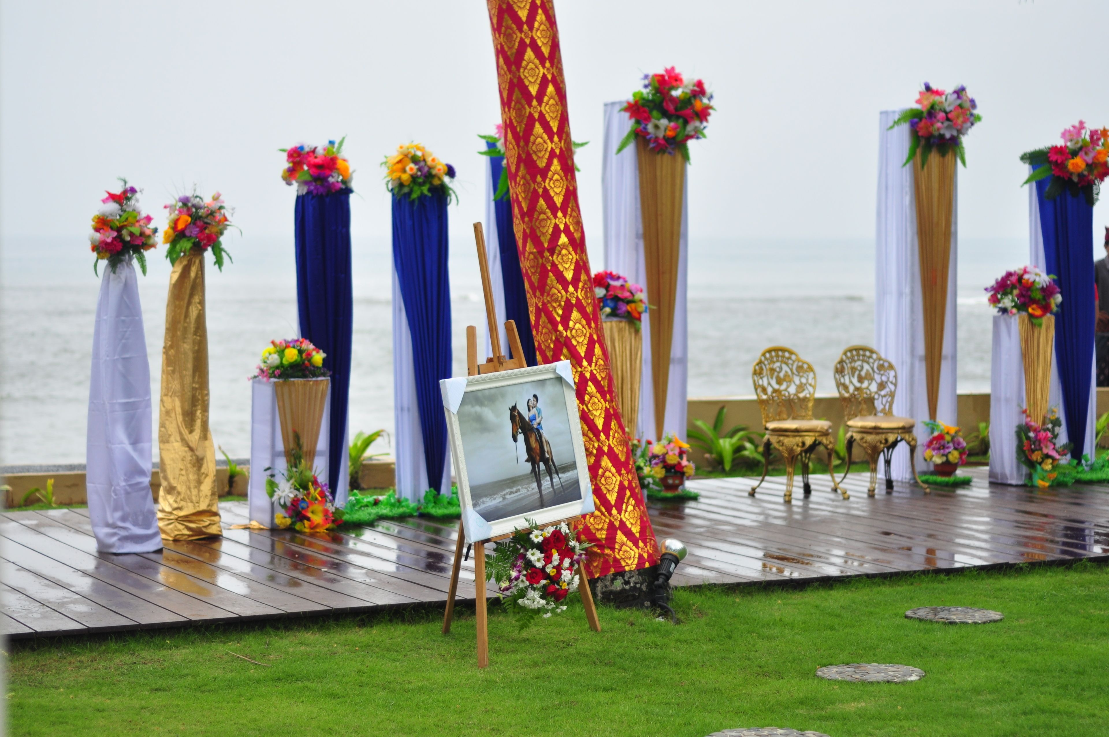 A stage with a wooden floor, decorated with floral arrangements and a framed photo.
