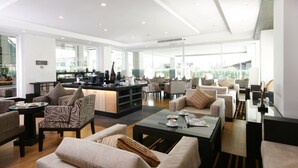 Un amplio salón con diversas opciones de asientos, una estación de café central y ventanas grandes que permiten la entrada de luz natural.