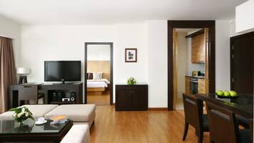 Habitación de hotel con televisor, sofá, mesa de centro y una kitchenette pequeña.