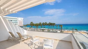 A balcony with white chairs and a view of the beach and ocean.