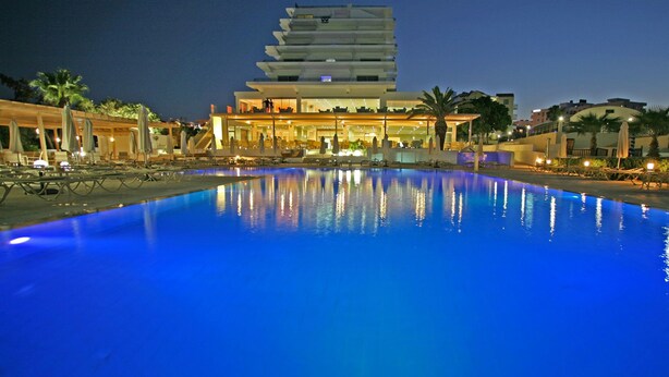 A modern hotel with a large swimming pool, outdoor seating, and a multi-story building. - Vrissiana Boutique Beach Hotel (Paralimni)
